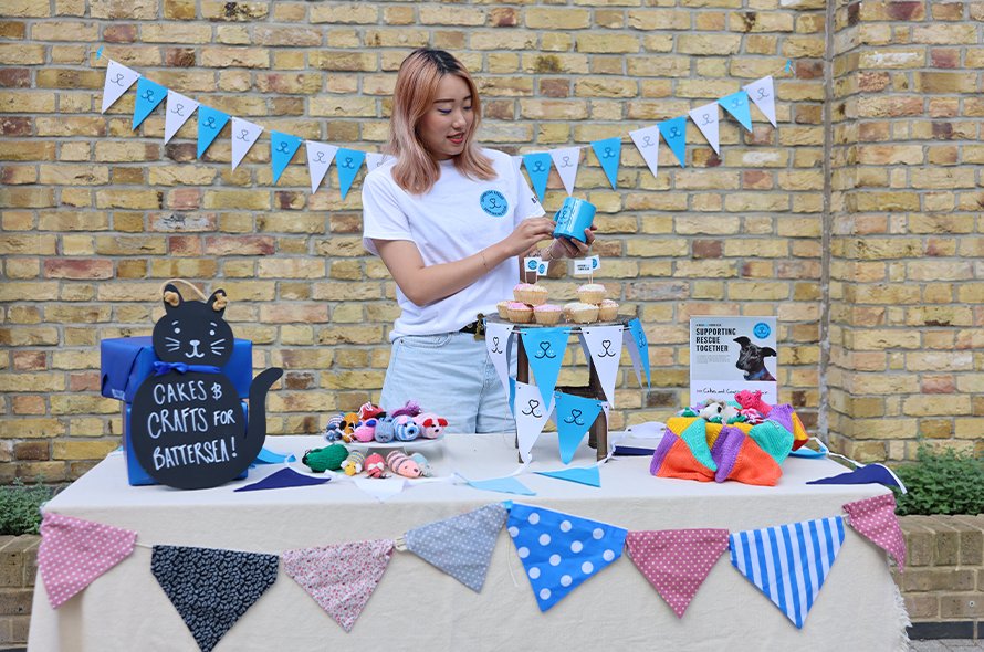 A person standing behind a cake and crafts sale