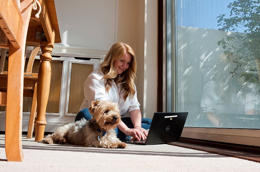 Woman working on computer with dog sitting next to her